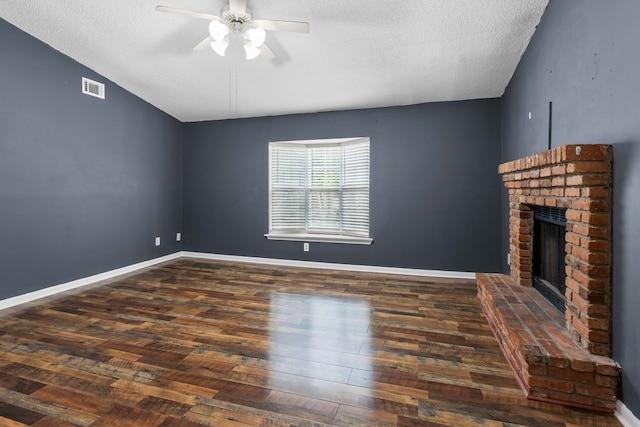 unfurnished living room with a brick fireplace, wood finished floors, visible vents, a textured ceiling, and ceiling fan