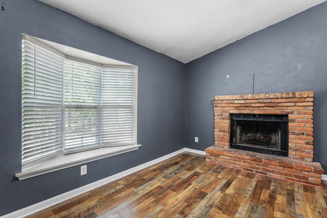 unfurnished living room with vaulted ceiling, baseboards, a brick fireplace, and hardwood / wood-style flooring