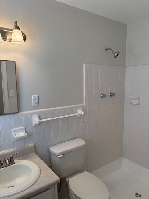 full bathroom featuring tile walls, a tile shower, vanity, a wainscoted wall, and toilet