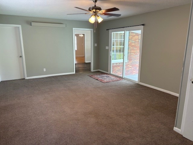 spare room featuring baseboards, carpet, ceiling fan, and a wall unit AC