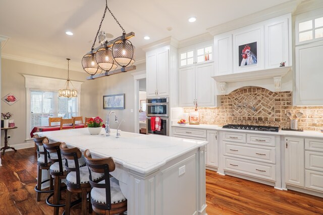 kitchen with dark wood-type flooring, stainless steel appliances, pendant lighting, a center island with sink, and white cabinets