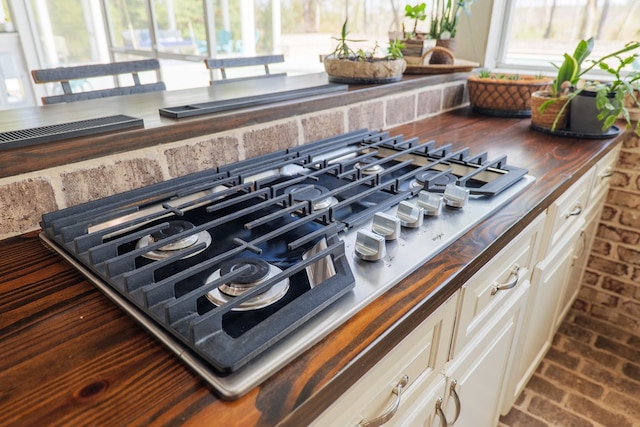 details with butcher block countertops, white cabinetry, and stainless steel gas stovetop