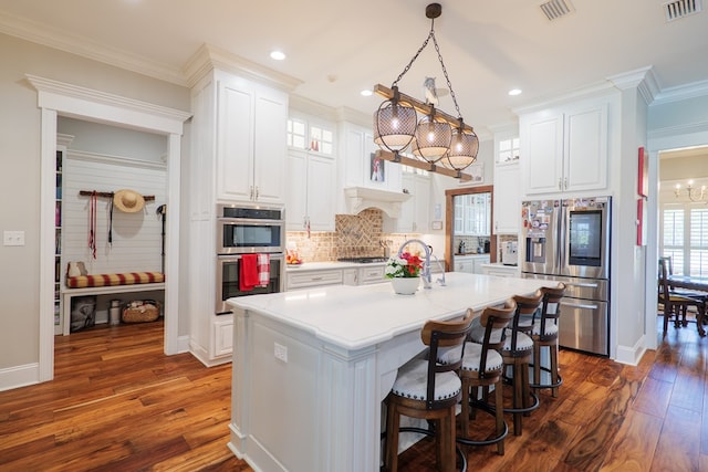 kitchen featuring dark wood-type flooring, stainless steel appliances, crown molding, decorative light fixtures, and white cabinets