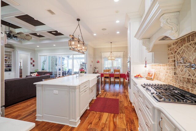 kitchen with stainless steel gas cooktop, hardwood / wood-style floors, pendant lighting, a center island with sink, and ornamental molding