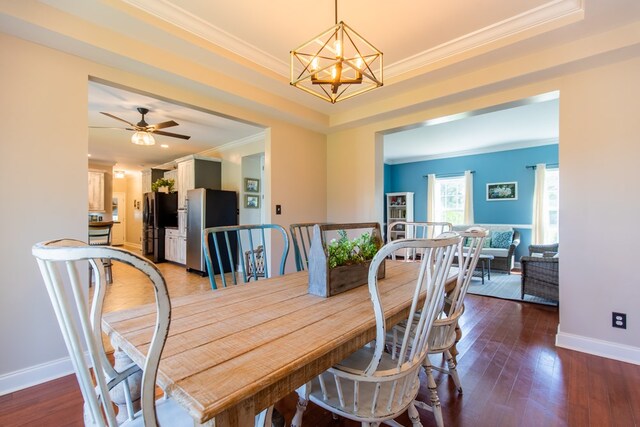 dining area with a raised ceiling, ceiling fan with notable chandelier, dark hardwood / wood-style flooring, and ornamental molding