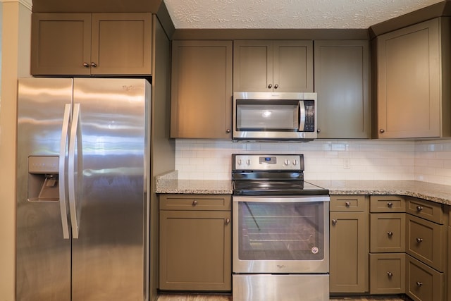 kitchen featuring light stone countertops, backsplash, gray cabinetry, a textured ceiling, and stainless steel appliances