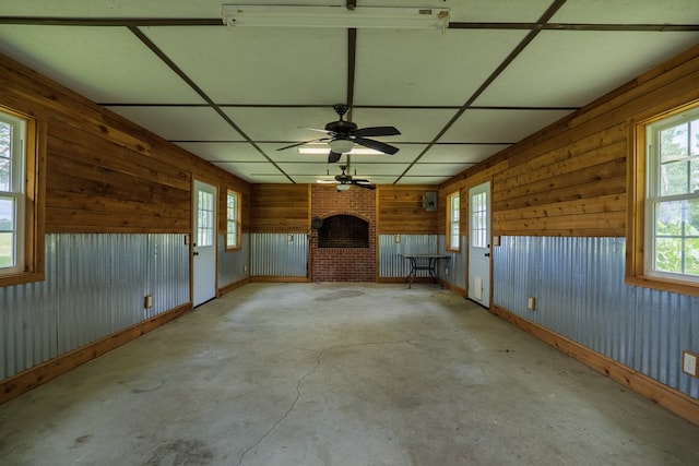 interior space with ceiling fan, wood walls, a drop ceiling, and a fireplace