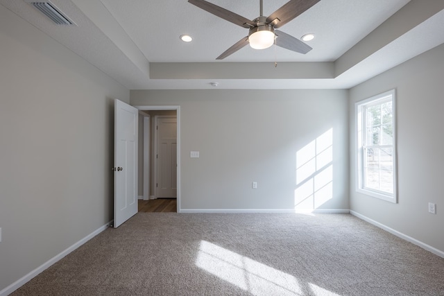 unfurnished room featuring carpet floors, a raised ceiling, visible vents, a ceiling fan, and baseboards