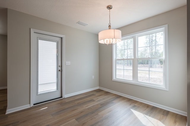 unfurnished dining area featuring baseboards, a textured ceiling, visible vents, and dark wood-type flooring