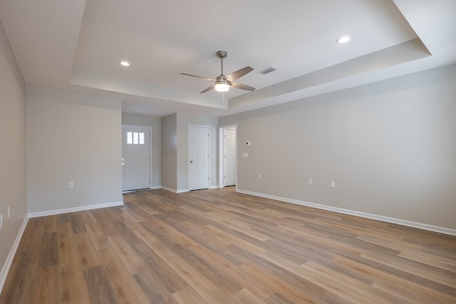 unfurnished room with a raised ceiling, visible vents, light wood-style flooring, and baseboards