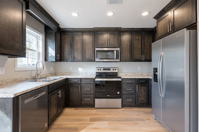 kitchen with stainless steel appliances, light wood-style floors, a sink, and dark brown cabinetry