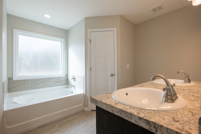 bathroom with double vanity, visible vents, a sink, and a bath