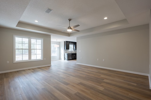 unfurnished living room with a tray ceiling, visible vents, dark wood finished floors, and baseboards