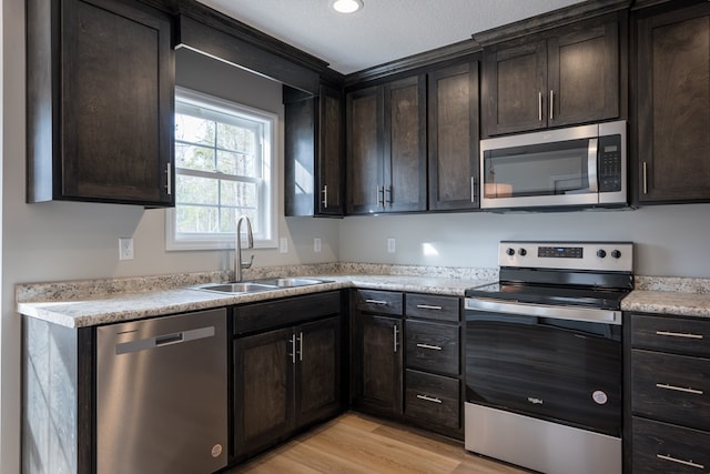 kitchen featuring light wood-style floors, appliances with stainless steel finishes, dark brown cabinets, and a sink