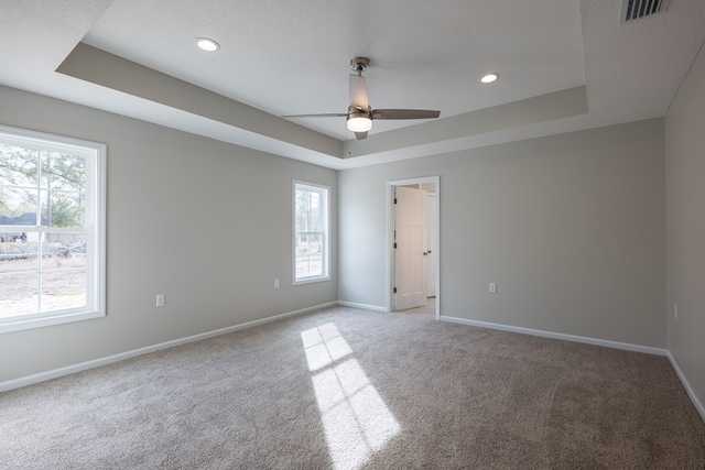 spare room featuring light colored carpet, a raised ceiling, visible vents, and baseboards