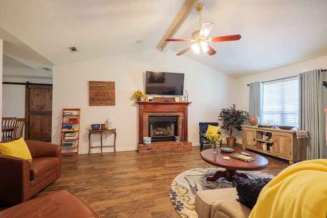 living room with ceiling fan, dark wood-type flooring, a brick fireplace, a barn door, and lofted ceiling with beams