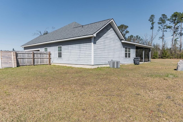 view of property exterior featuring cooling unit, a lawn, a shingled roof, and fence