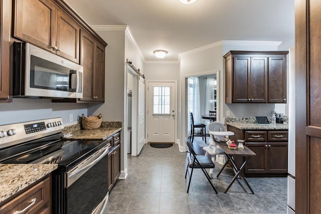 kitchen with light stone counters, dark brown cabinets, appliances with stainless steel finishes, and a barn door