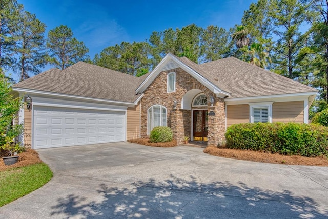 view of front of property featuring a shingled roof, an attached garage, concrete driveway, and stone siding