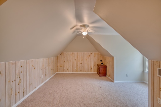 additional living space with baseboards, wood walls, a ceiling fan, and lofted ceiling