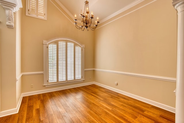 empty room featuring decorative columns, hardwood / wood-style flooring, baseboards, a notable chandelier, and ornamental molding