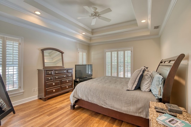 bedroom featuring visible vents, crown molding, baseboards, a tray ceiling, and light wood-style flooring