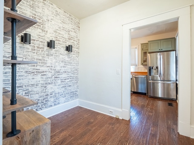 interior space with brick wall, visible vents, baseboards, and dark wood-style flooring