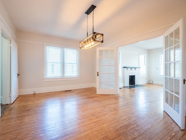 interior space featuring a brick fireplace, french doors, light wood-style flooring, and baseboards