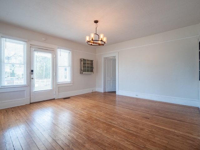 unfurnished room with an inviting chandelier, visible vents, baseboards, and wood finished floors