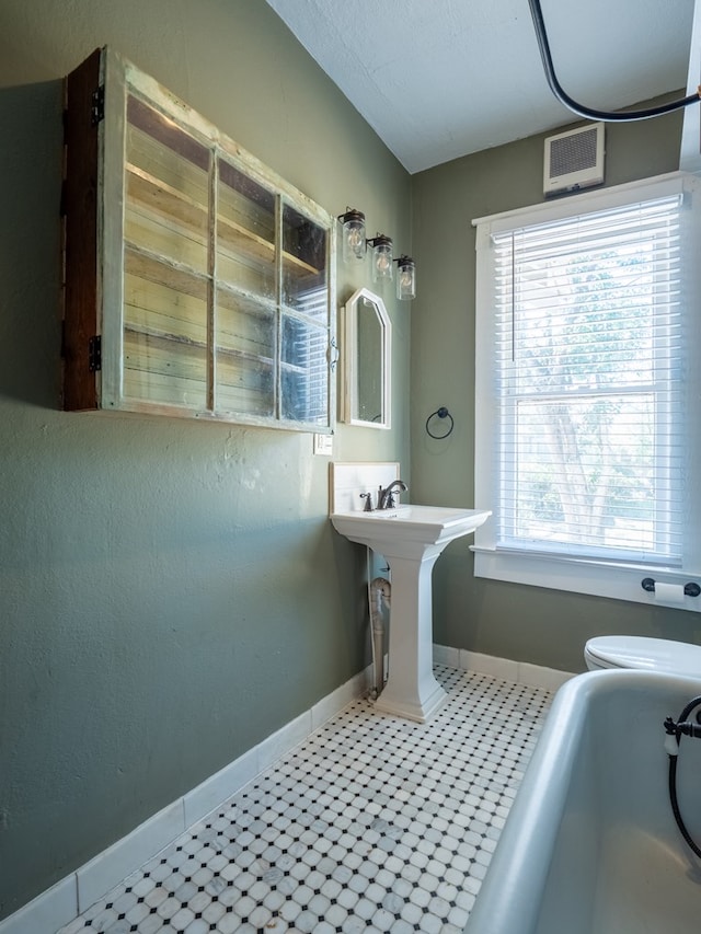 bathroom featuring lofted ceiling, a tub, baseboards, and toilet