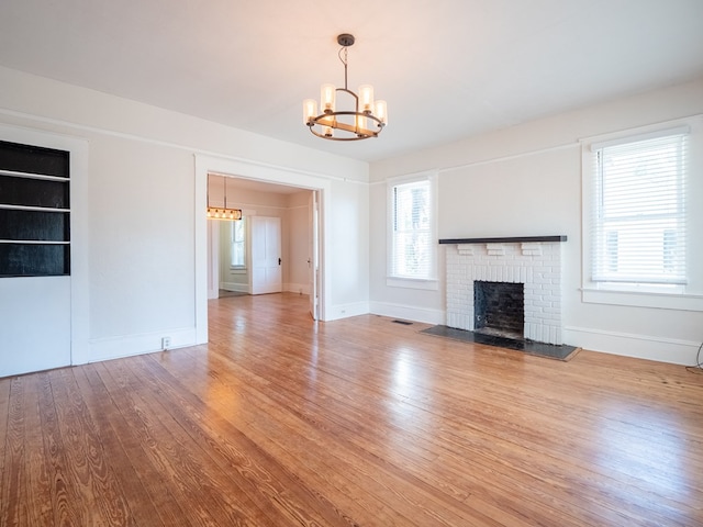 unfurnished living room with a chandelier, a fireplace, wood finished floors, and baseboards