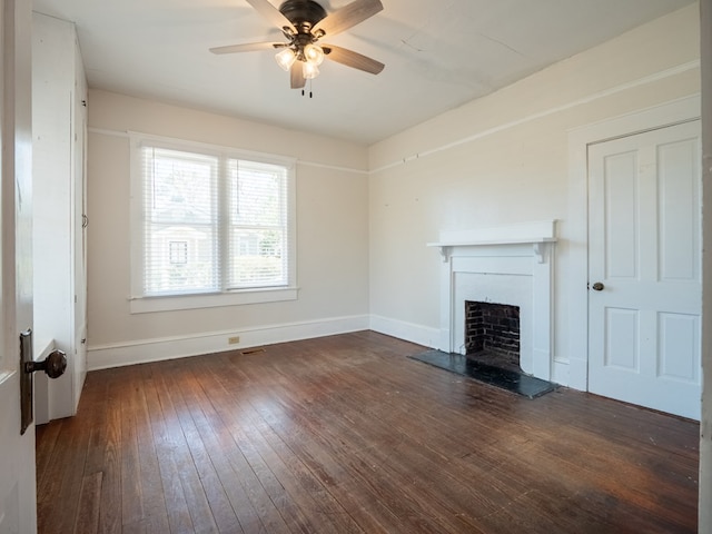 unfurnished living room featuring dark wood-style floors, baseboards, a fireplace with raised hearth, and a ceiling fan