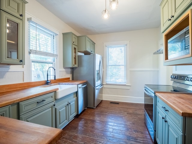 kitchen featuring wood counters, glass insert cabinets, appliances with stainless steel finishes, dark wood-style flooring, and a sink