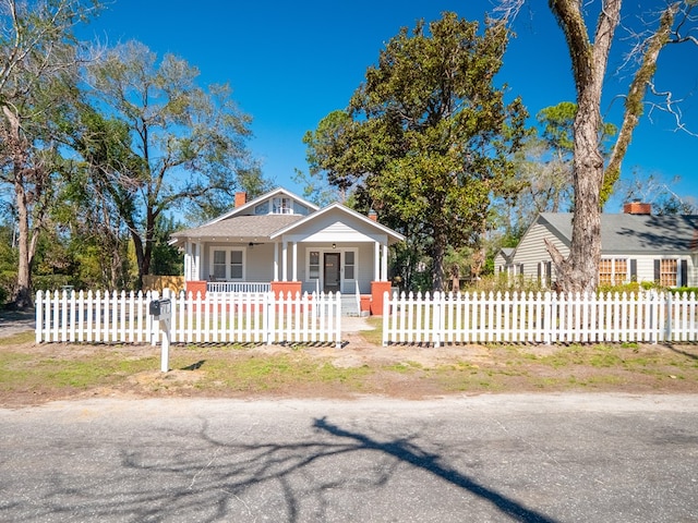 bungalow with a fenced front yard, covered porch, and a chimney