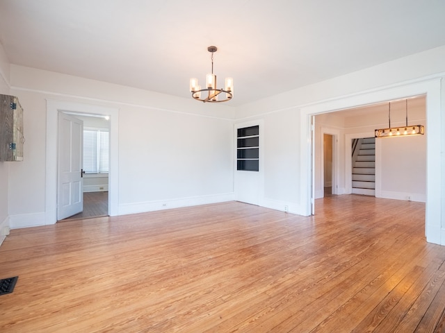 unfurnished room featuring an inviting chandelier, stairs, baseboards, and light wood finished floors