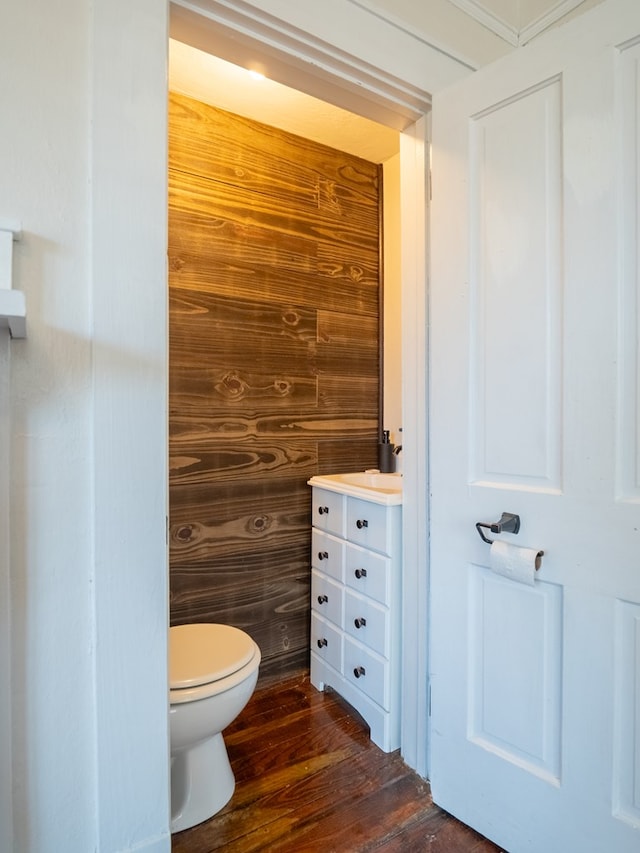 half bathroom with vanity, wooden walls, toilet, and wood finished floors