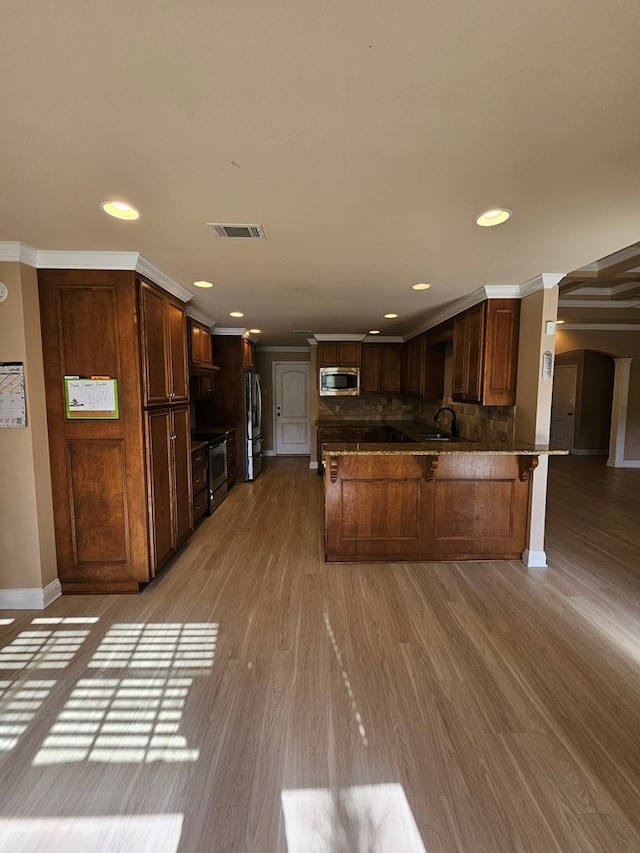 kitchen featuring kitchen peninsula, appliances with stainless steel finishes, decorative backsplash, ornamental molding, and light hardwood / wood-style flooring