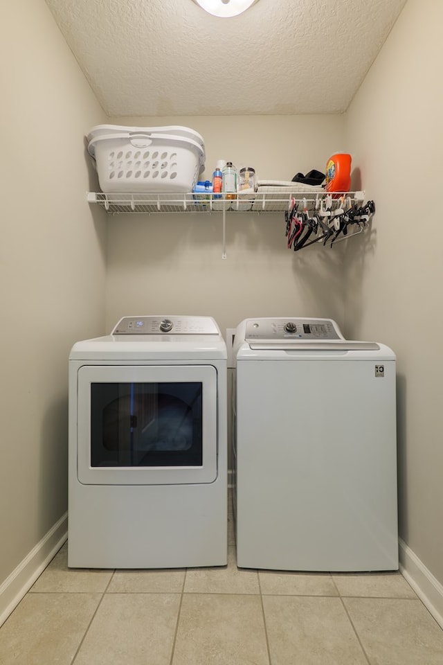 laundry area with light tile patterned floors, a textured ceiling, and washing machine and clothes dryer