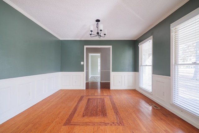 spare room featuring visible vents, wainscoting, a textured ceiling, light wood-type flooring, and a chandelier