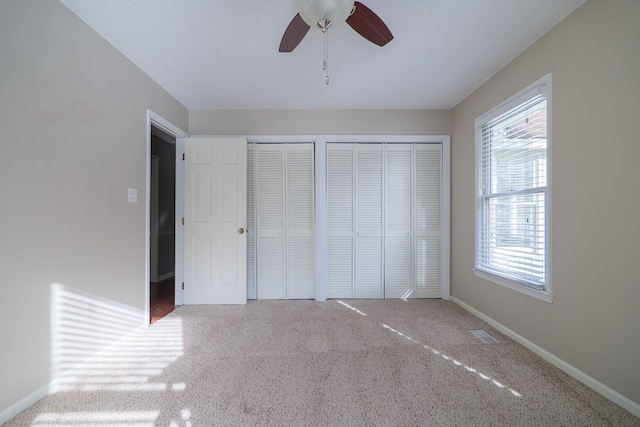 unfurnished bedroom with carpet, two closets, visible vents, ceiling fan, and baseboards