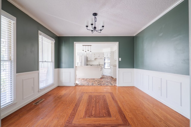 unfurnished dining area featuring a wainscoted wall, light wood finished floors, visible vents, an inviting chandelier, and a textured ceiling