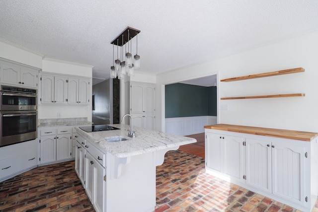 kitchen with a center island with sink, wainscoting, double oven, pendant lighting, and a sink