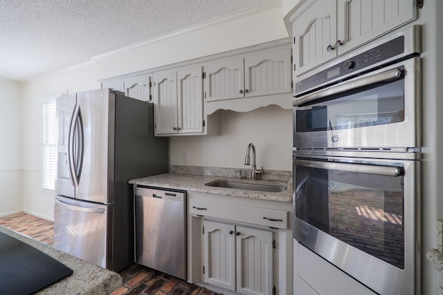 kitchen with appliances with stainless steel finishes, ornamental molding, light countertops, a textured ceiling, and a sink