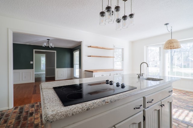 kitchen featuring a center island with sink, wainscoting, hanging light fixtures, black electric cooktop, and a sink