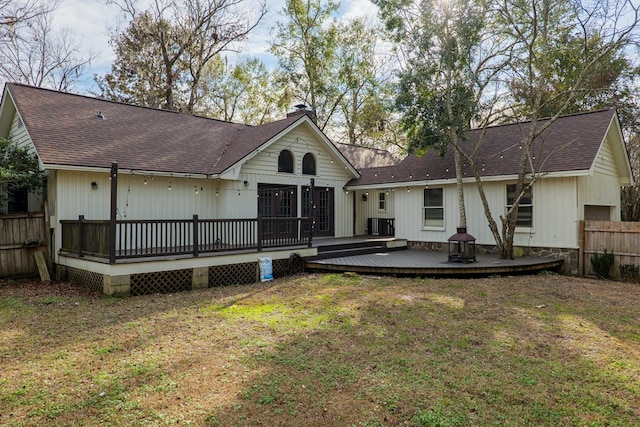 rear view of house with a deck, a chimney, fence, and a lawn