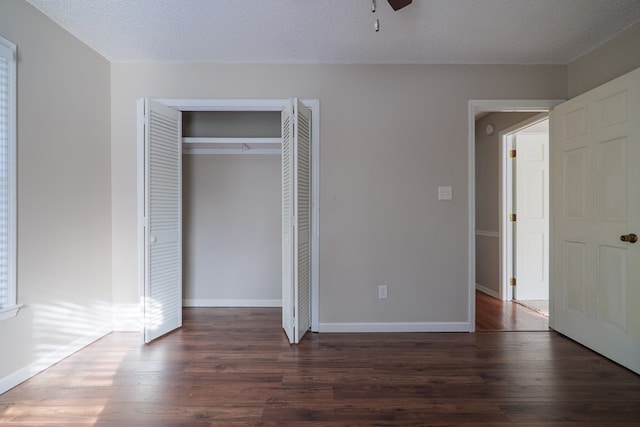 unfurnished bedroom with a textured ceiling, dark wood-type flooring, a closet, and baseboards