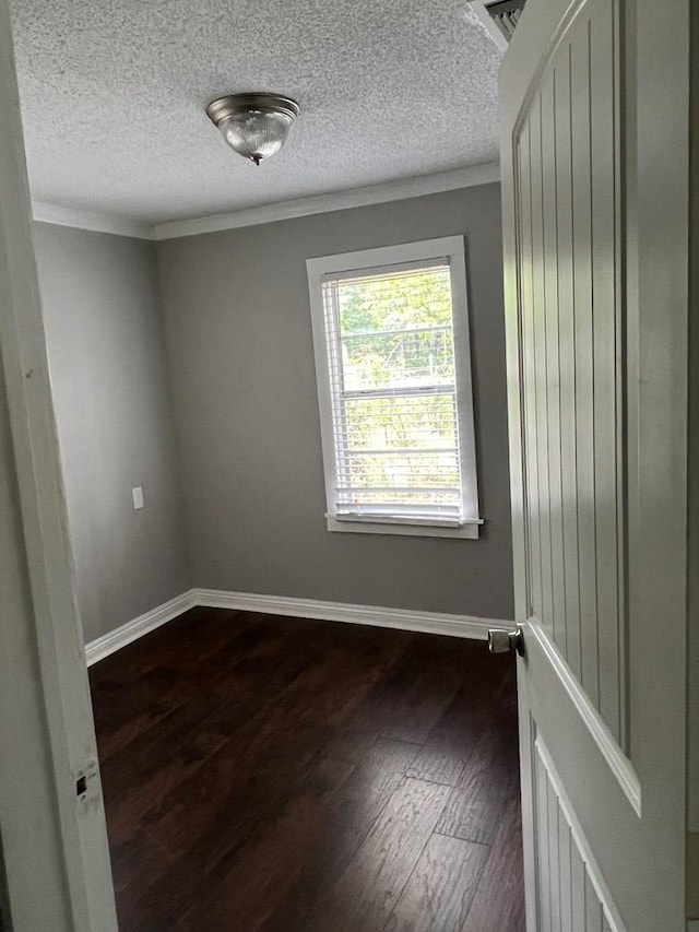 empty room with ornamental molding, a textured ceiling, and dark wood-type flooring