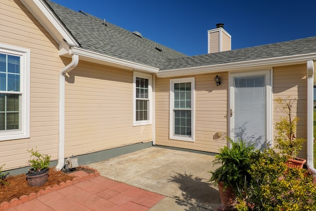 view of exterior entry with a patio area, a chimney, and a shingled roof