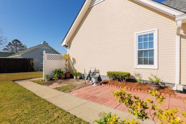 view of property exterior featuring a patio, a lawn, a shingled roof, and fence