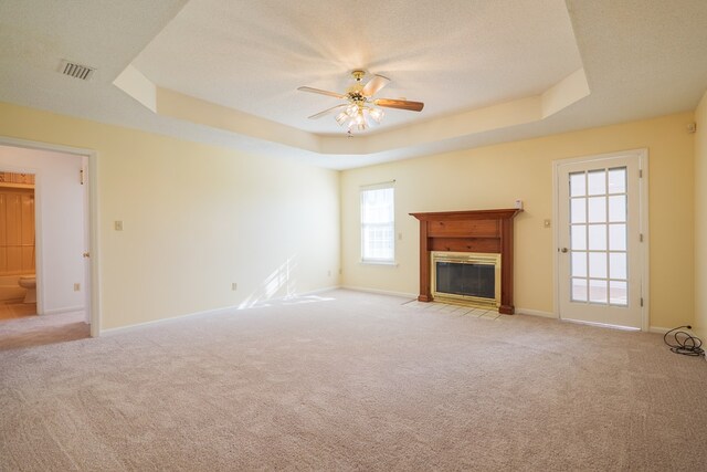 unfurnished living room with visible vents, light carpet, a fireplace with flush hearth, a ceiling fan, and a raised ceiling